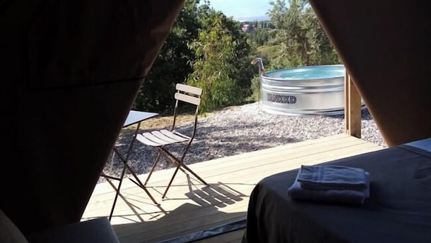 Una tienda acogedora con una cama, una silla, un jacuzzi y vistas del follaje circundante.