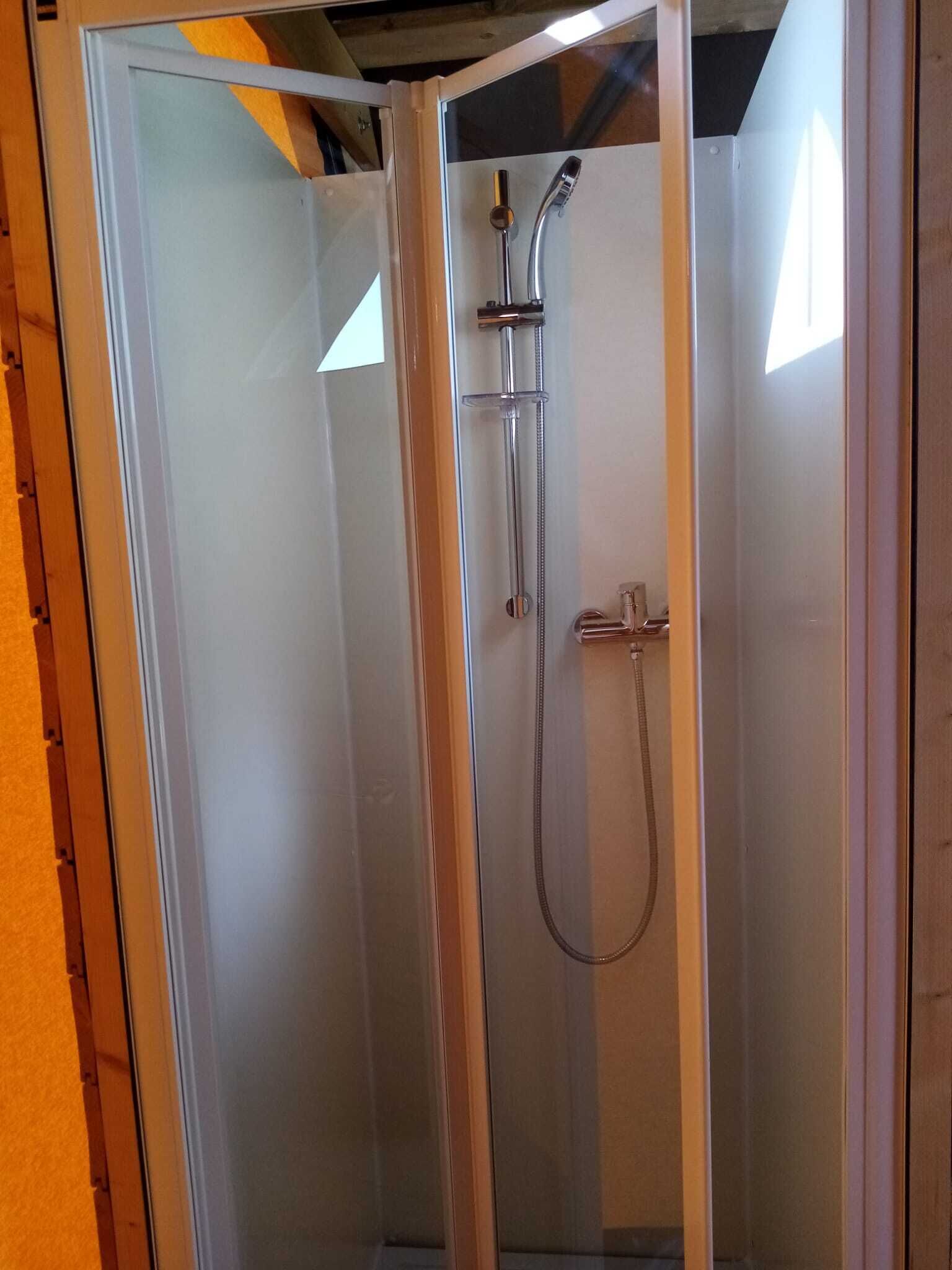 A glass-enclosed shower stall with a handheld showerhead and a handheld faucet.