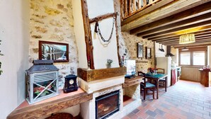 Un interior rústic amb parets de pedra vista, un sostre de fusta, una llar de foc i una zona de menjador amb taula i cadires.