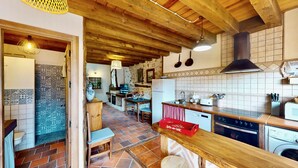 Una cuina rústica amb bigues de fusta, un frontó de rajola i una zona de menjador amb taula i cadire.