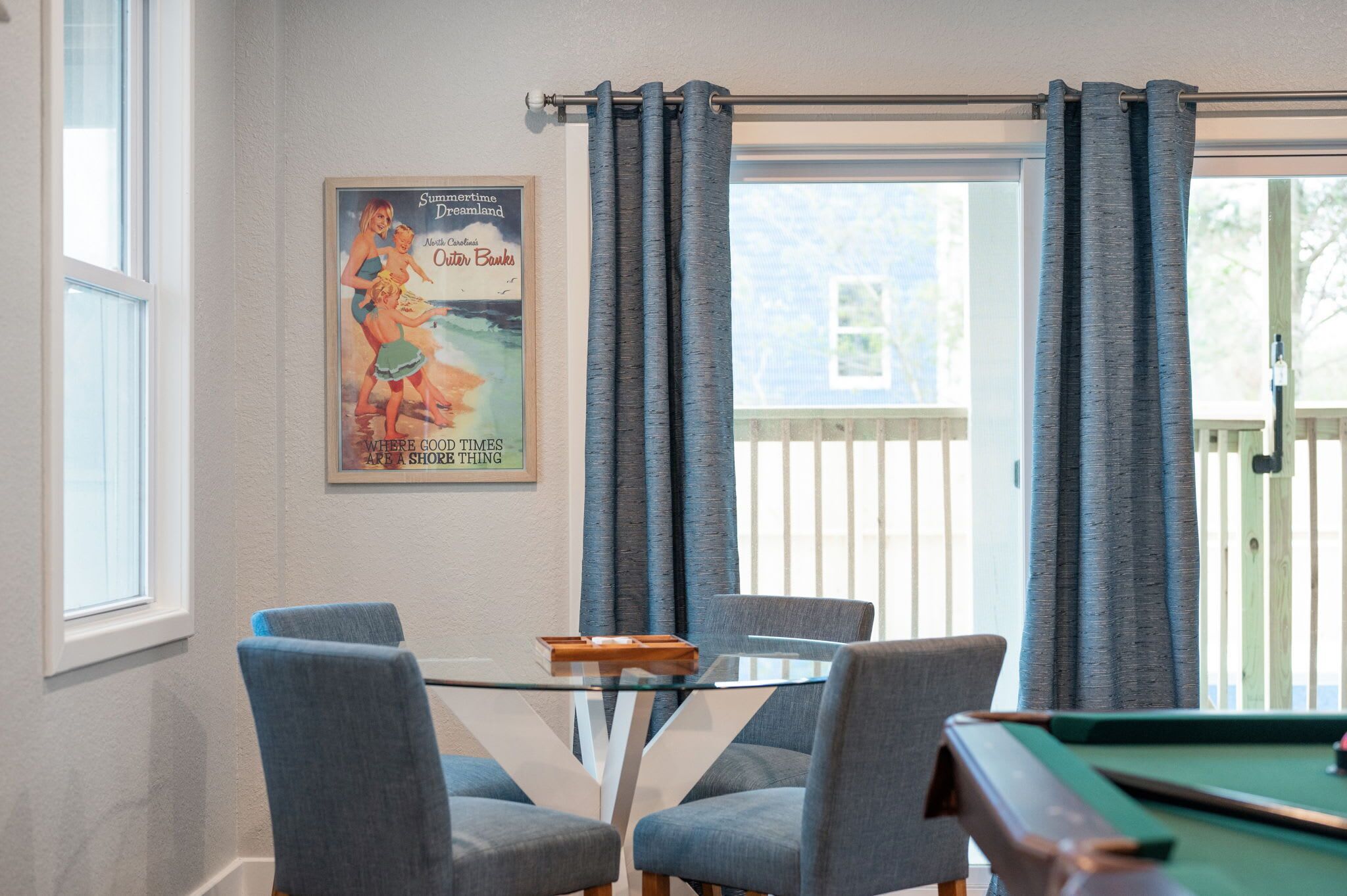 Une pièce avec une table dont le plateau est en verre, entourée de quatre chaises, une table de billard et une affiche accrochée au mur.