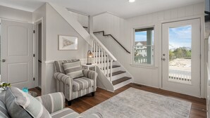 A living room with a striped armchair, a staircase, and a door leading outside. - Luxury Home Near Beach with Pool, Spa! (Corolla)