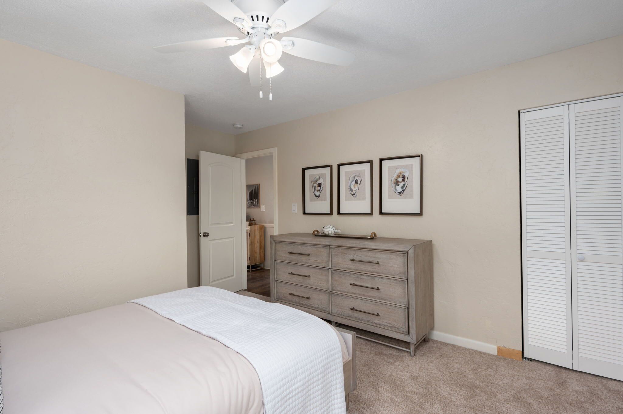 A bedroom with a bed, a dresser, a closet, and a ceiling fan.