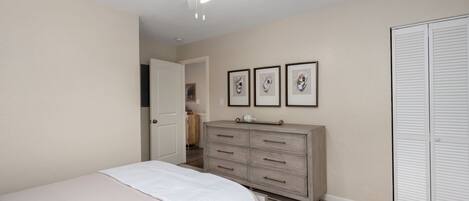 A bedroom with a bed, a dresser, a closet, and a ceiling fan.