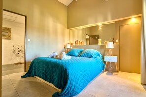 A bedroom with a large bed, a bedside table, a nightstand, a mirror, and a wall-mounted shelf with decorative items. - Mas au Coeur du Luberon Avec Piscine à Débordement12x4m (Apt)