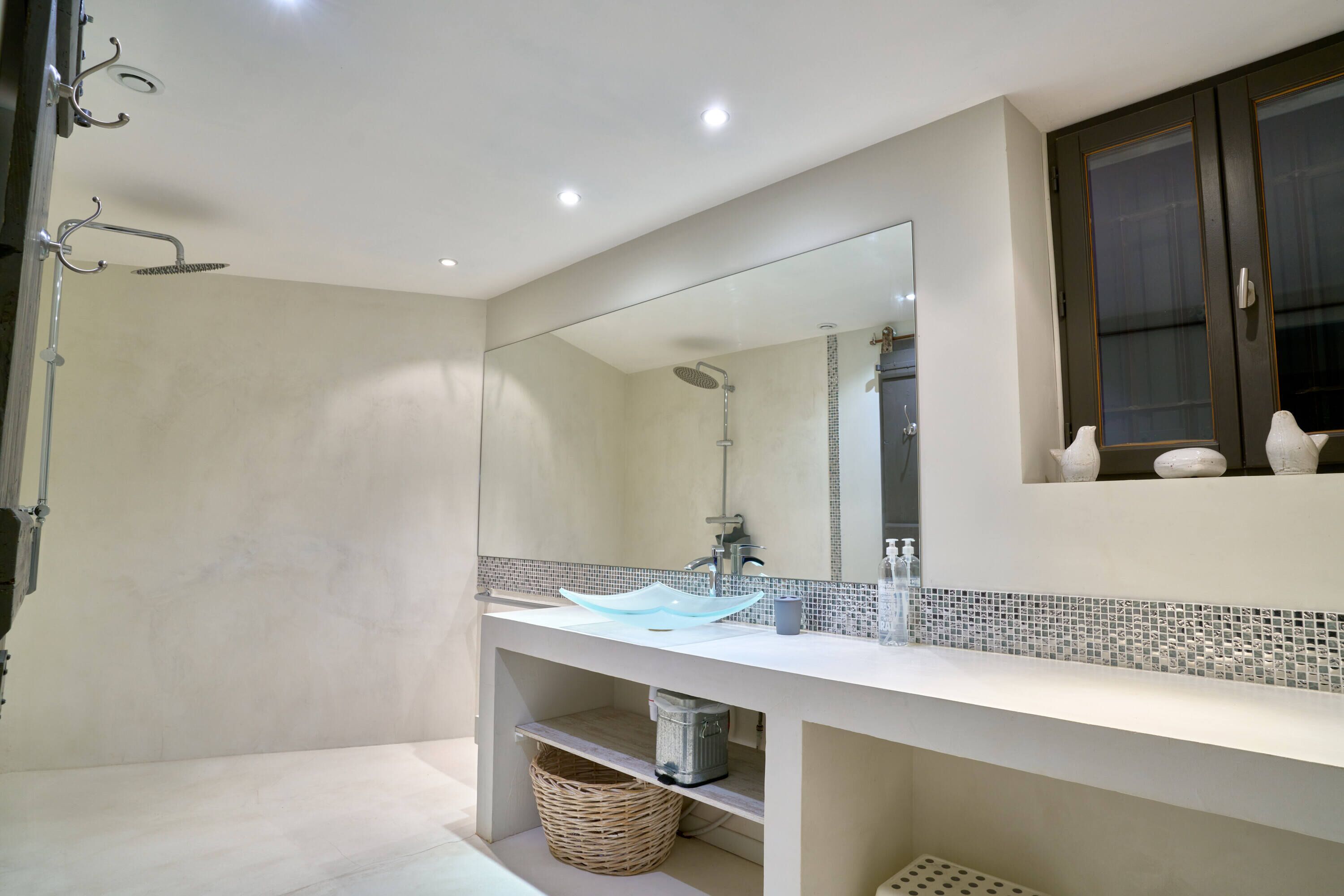 Un baño moderno con un espejo grande, un lavabo de cristal y una ducha.