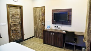 Ein Hotelzimmer mit Holztür, Wandfernseher, Schreibtisch mit Stuhl und Bett.