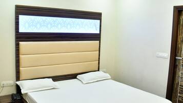 Ein kleines, ordentlich eingerichtetes Schlafzimmer mit einem Bett, einem Fenster mit Jalousien, einem Deckenventilator und einer Steckdose an der Wand.