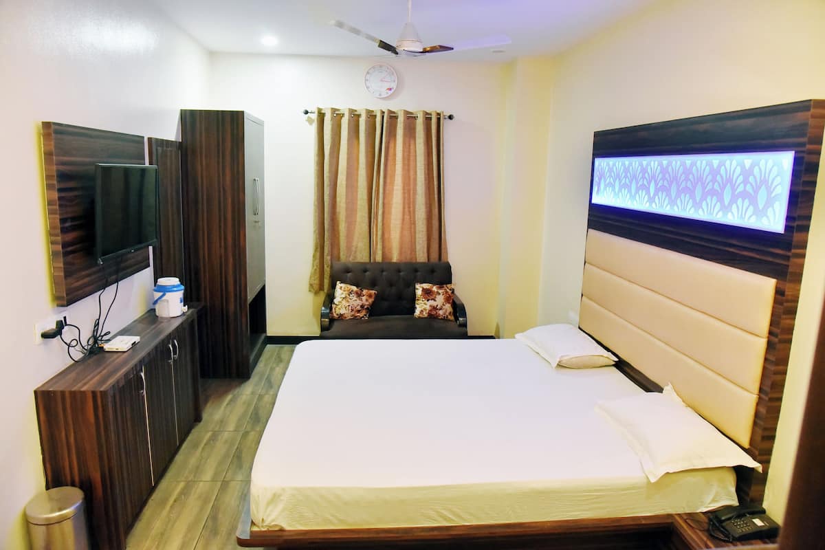 Una habitación de hotel con una cama, un televisor montado en la pared, un armario de madera, un ventilador de techo y una cortina.