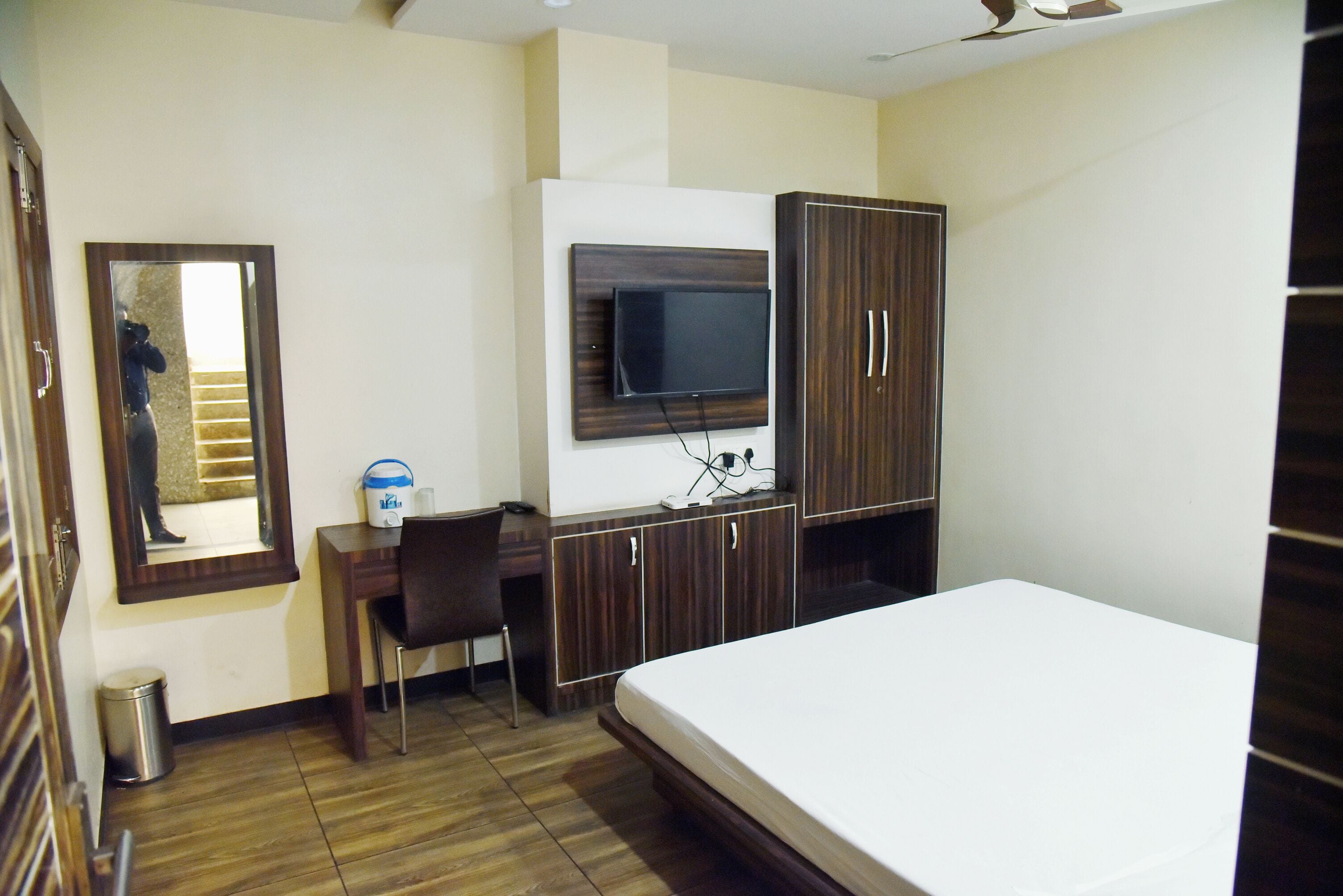 A bedroom with a bed, a desk, a chair, a TV mounted on the wall, and a wardrobe.