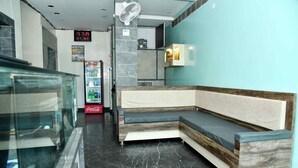 Eine moderne Lobby mit einer Rezeption, einer digitalen Uhr, einem Coca-Cola-Kühlschrank und einer Sitzecke mit einer Holzbank und gepolsterten Sitzgelegenheiten.