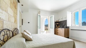 A bedroom with a bed, a stone wall, a kitchen area, and a view through an open door. - 3843 Petricore - Trilocale by Barbarhouse (Nardò)
