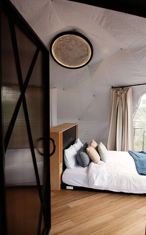 A bedroom with a bed, pillows, a bedside table, and a hanging light fixture.
