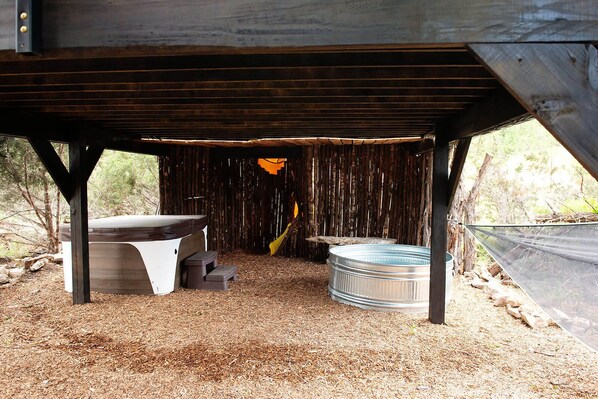 Un entorno rústico al aire libre con una terraza de madera, un depósito de agua metálico y un banco.