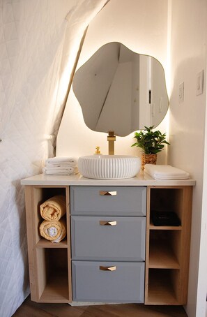 Un meuble-lavabo de salle de bain avec un grand miroir, un évier et une plante en pot. Des serviettes et une couverture pliée sont rangées dans le placard.