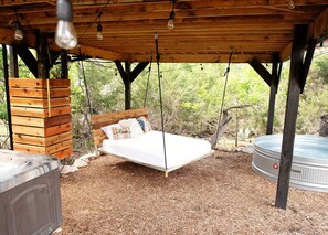 Un lit en bois placé sous une pergola illuminée de guirlandes lumineuses, un jacuzzi et une structure en bois sur la gauche.