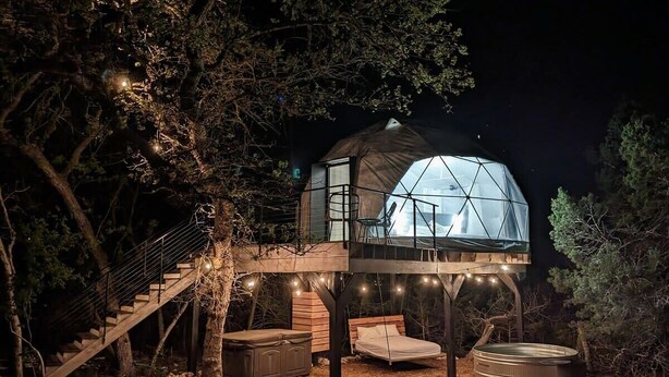 A treehouse with a glass dome, wooden deck, and a staircase leading up. - Treehouse!! Serenity Dome With Private Hot Tub! (Fredericksburg)