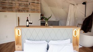 A bedroom with a bed, bedside table, and a small kitchenette area. - Treehouse!! Serenity Dome With Private Hot Tub! (Fredericksburg)