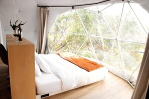 Une pièce avec un lit, un bureau en bois et une grande fenêtre donnant sur les arbres.