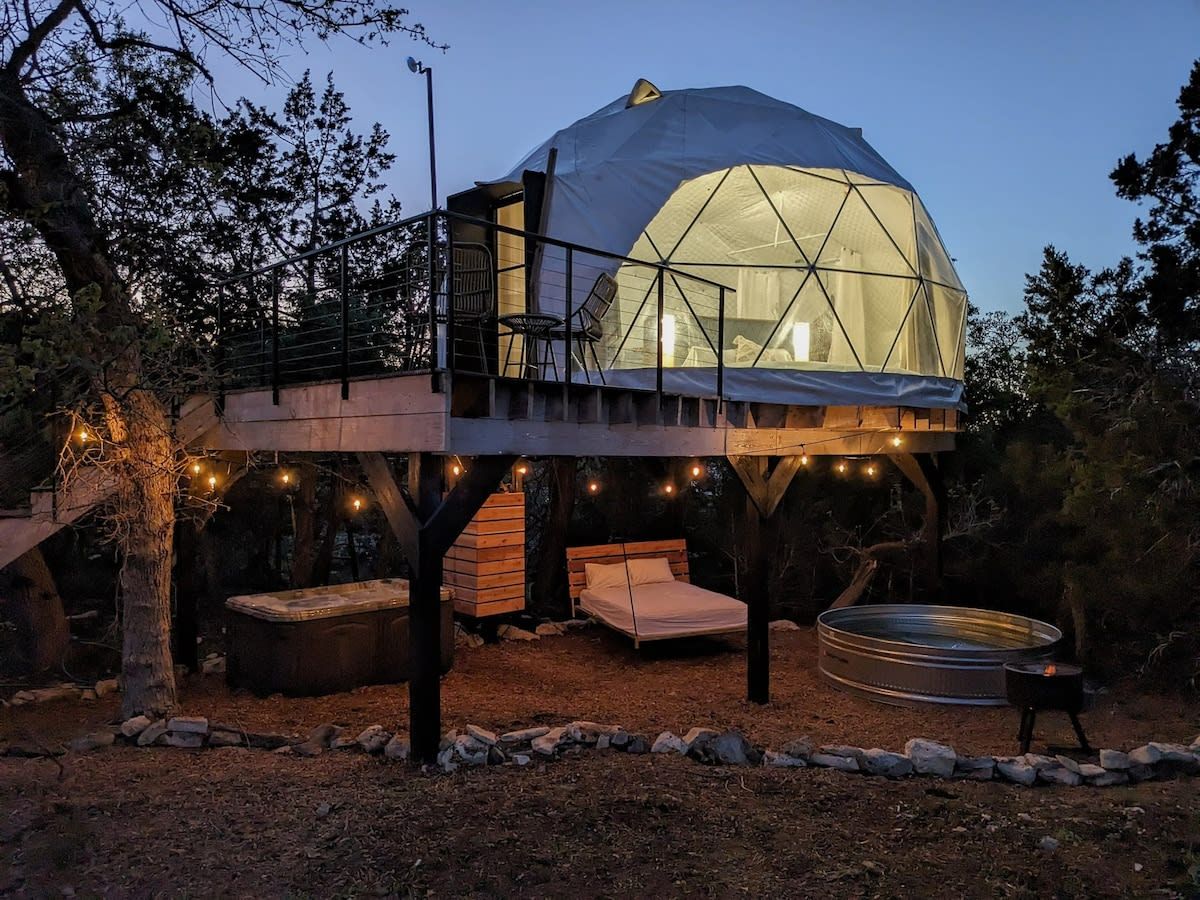 A geodesic dome structure with a bed, seating area, and hot tub.