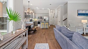 A modern kitchen with a central island, a dining area with a wooden bench, and a living room with a sofa and a lamp. - Dog-Friendly Home with Community Pools (Santa Rosa Beach)