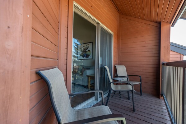 A wooden deck with two chairs and a glass door leading to a room. - Cozy 4BR Ski Condo | Ski Shuttle + Fireplace (Steamboat Springs)