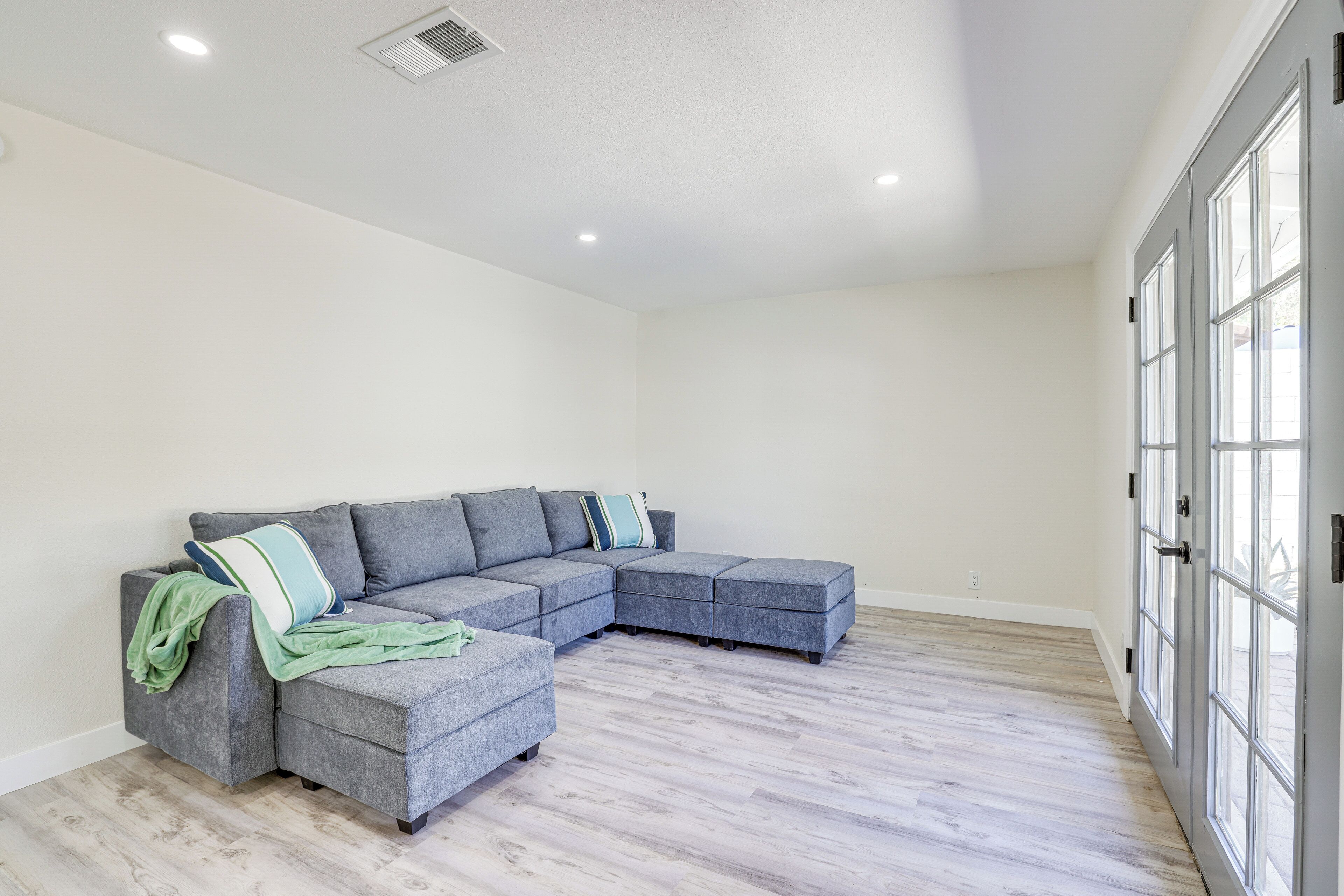 A spacious living room with a grey sectional sofa, a green throw blanket, and a large window with multiple panes.