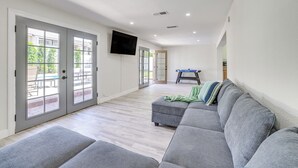A spacious living area with a grey sofa, a flat-screen TV mounted on the wall, and a ping pong table in the background. - Furnished Patio! Family-friendly Retreat in Tempe (Tempe)