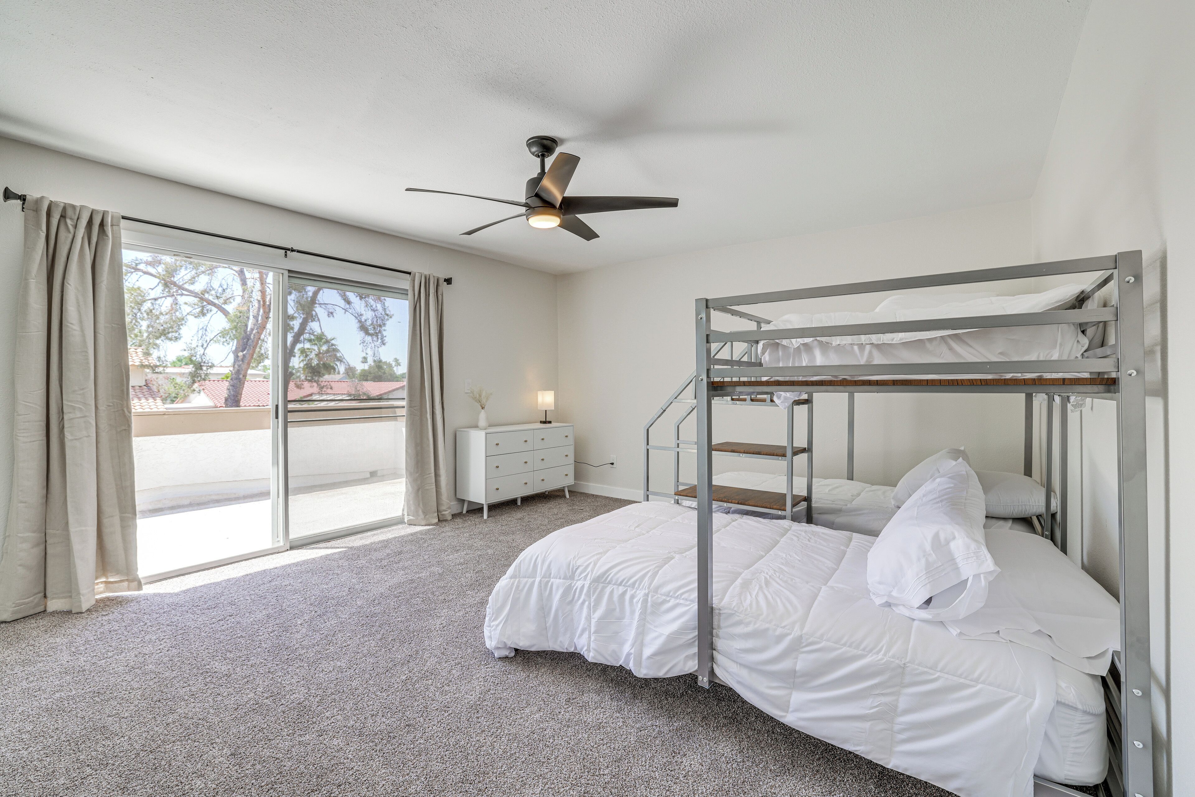 A room with a bunk bed, a ceiling fan, a dresser, and a sliding glass door leading to an outdoor area.