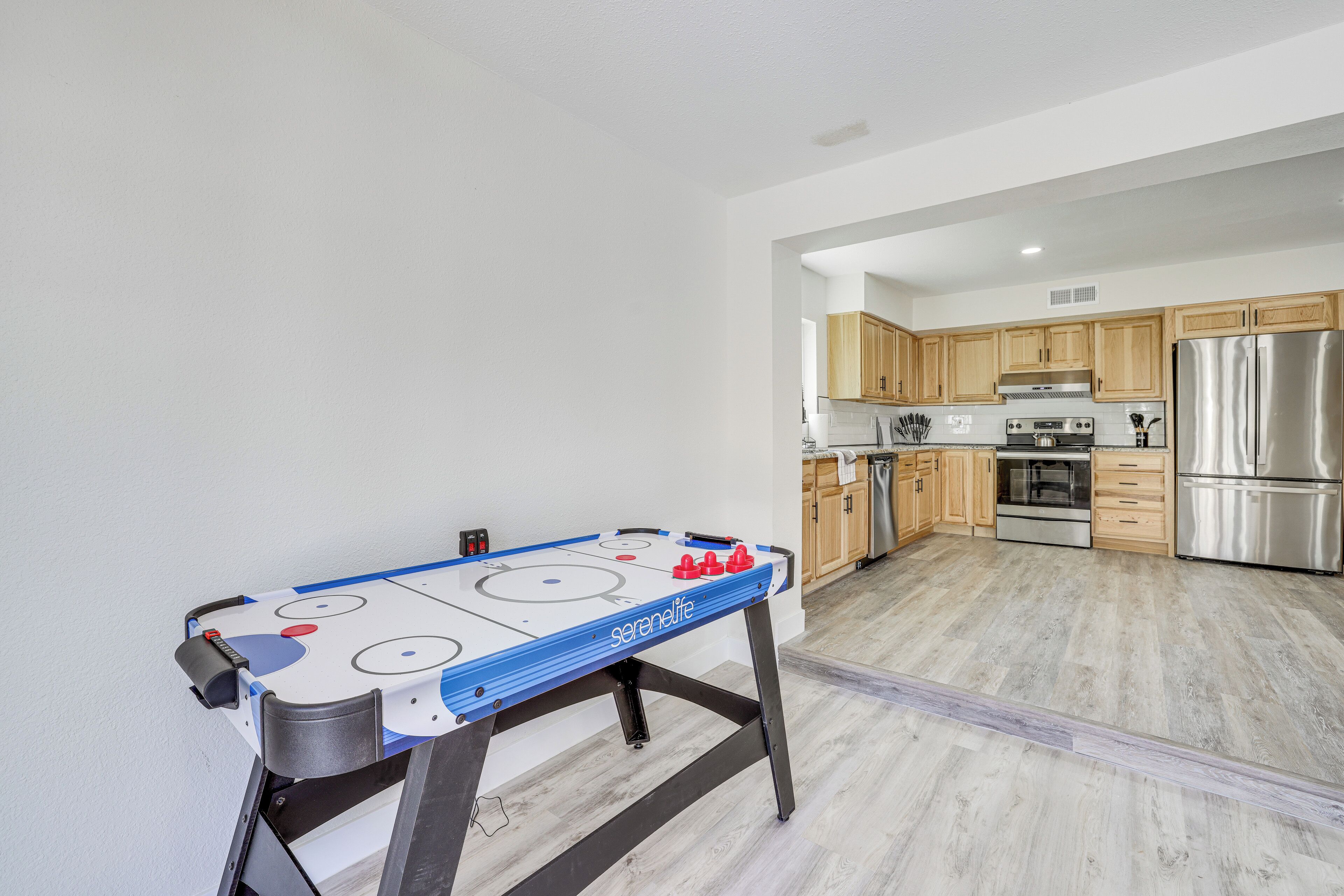 A modern kitchen with wooden cabinets, a stainless steel refrigerator, and a foosball table.