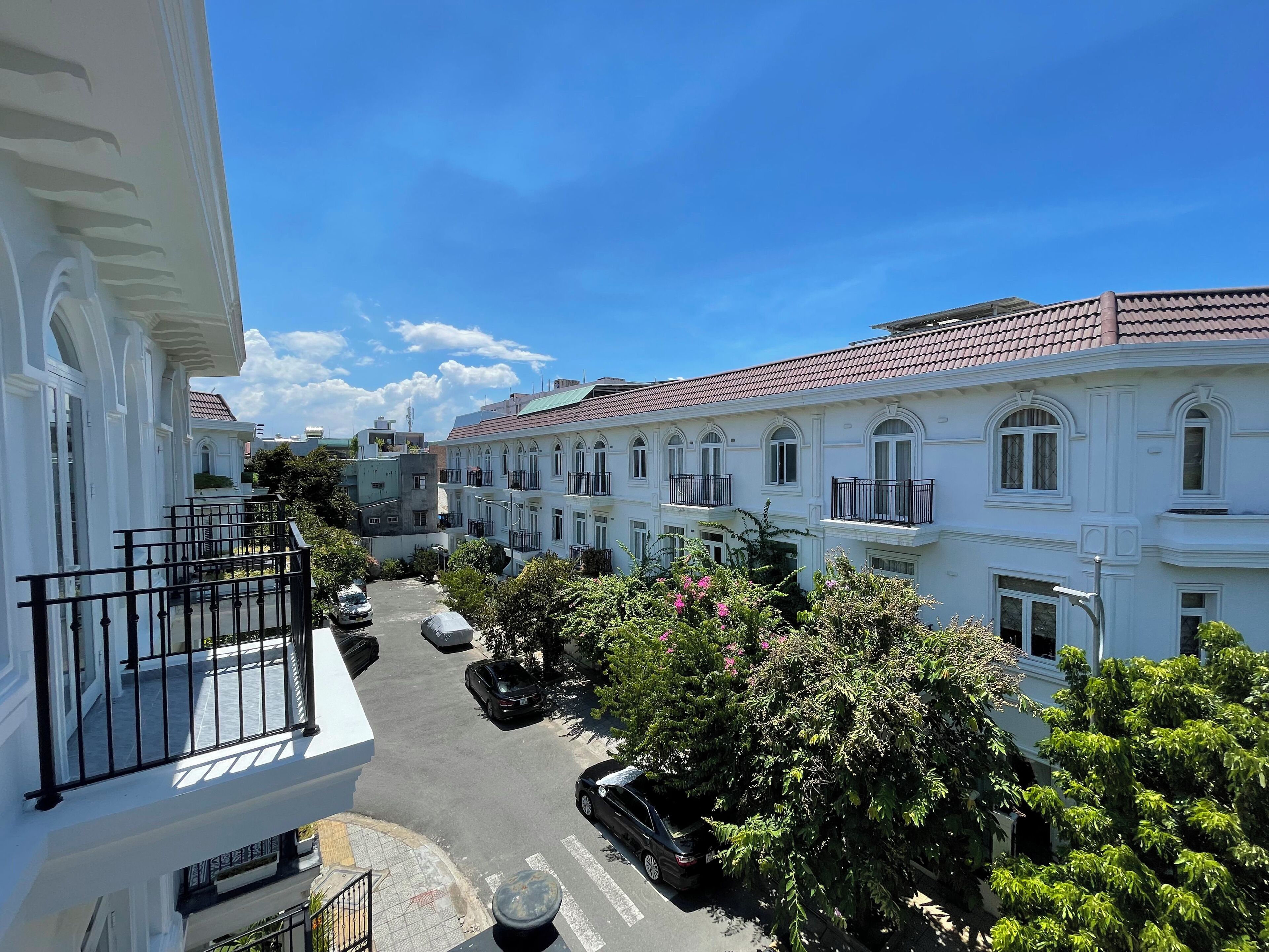 A narrow street lined with white buildings, featuring balconies and a clear blue sky.