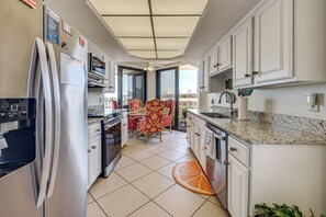 Eine Küche mit Kühlschrank, Mikrowelle und Backofen, ein Essbereich mit Stühlen und Blick durch die Glastür.