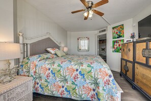 Ein Schlafzimmer mit einem Bett, einem Deckenventilator, einem Schminktisch und Kunstwerken an den Wänden.