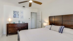 Une chambre à coucher avec un grand lit, une tête de lit en bois, deux lampes de chevet, une commode et des œuvres d’art accrochées au mur.