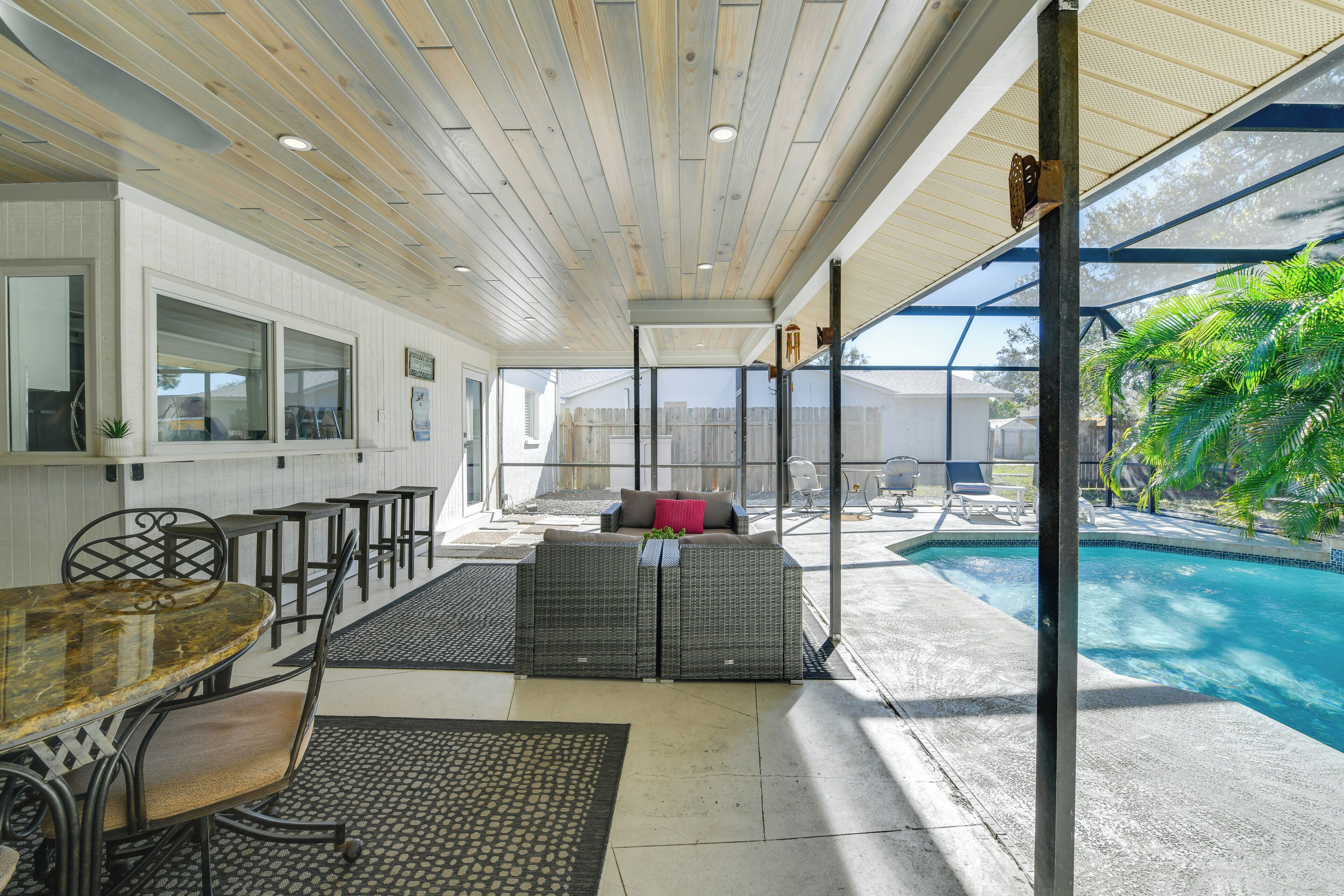 A covered outdoor seating area with a pool, wicker furniture, and a view of the backyard.