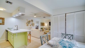 A modern kitchen with a central island, a dining area with a table set for four, and a living room with a sofa and decorative wall art.