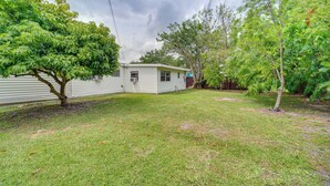 A single-story mobile home with a small attached garage, surrounded by a grassy yard and trees. - Vero Beach Studio w/ Shared Patio ~ 3 Mi to Beach! (Vero Beach)