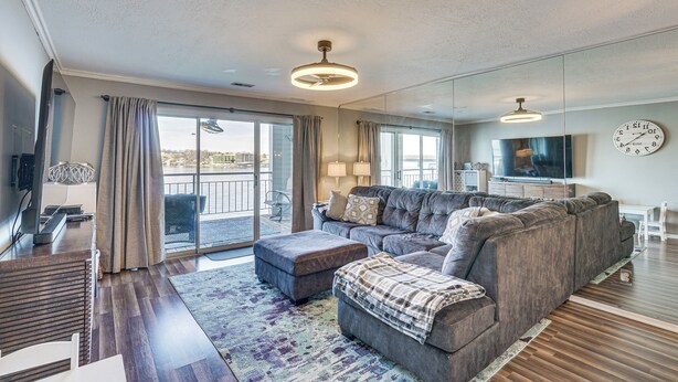 A modern living room with a sectional sofa, a flat-screen TV, and a large window with curtains. - Lakefront Retreat w/ Community Pool in Osage Beach (Osage Beach)