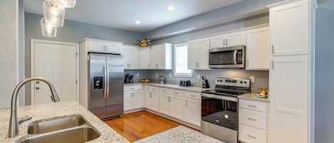 A modern kitchen with white cabinets, stainless steel appliances, granite countertops, and a wooden floor.