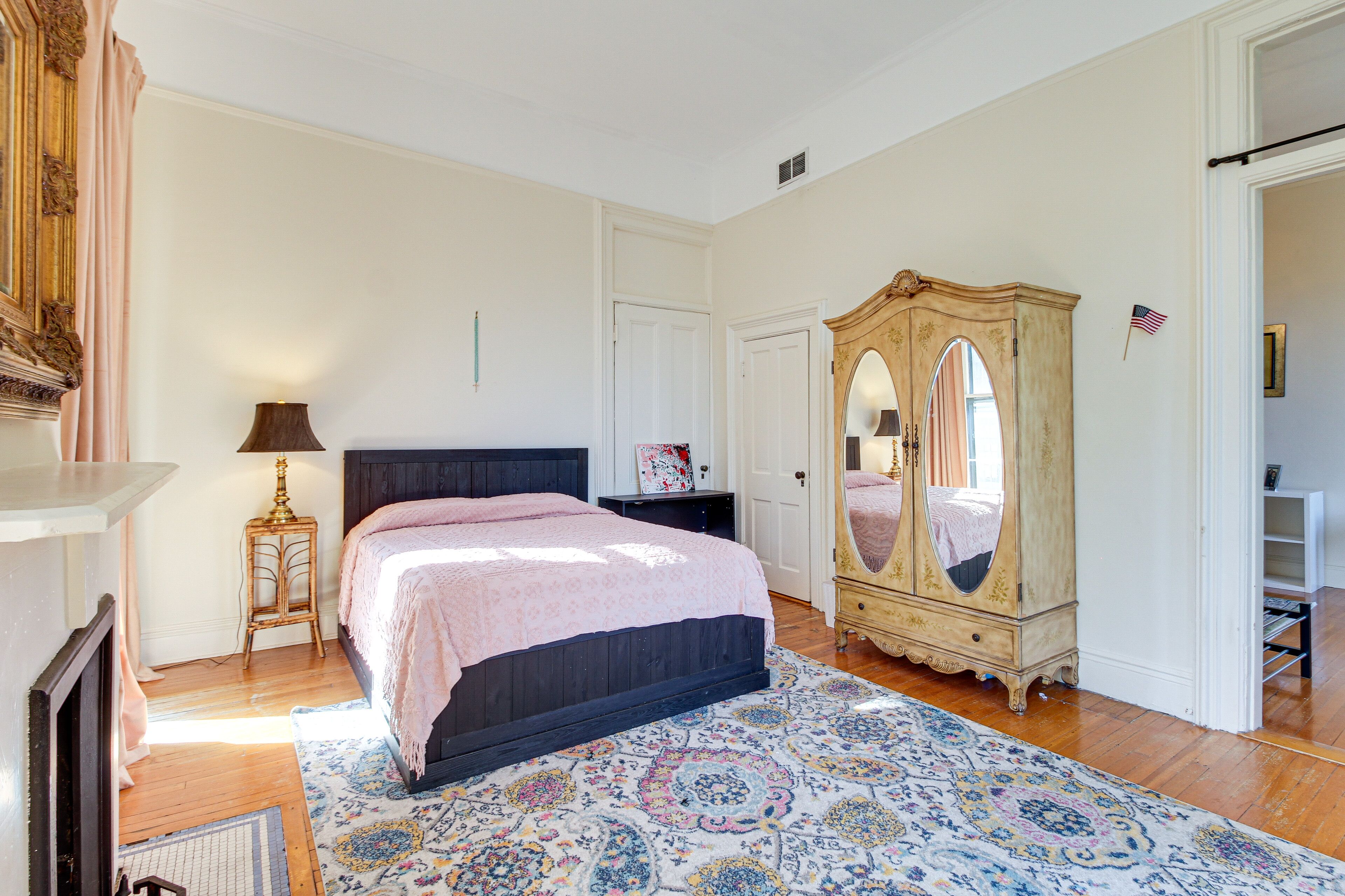 A bedroom with a bed, a dresser, a mirror, and a small table with a lamp.