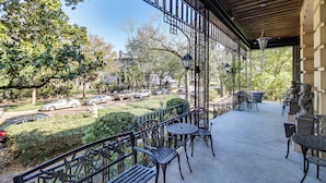 A covered outdoor seating area with metal chairs and tables, a stone statue, and a view of parked cars and trees.
