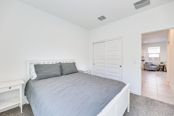 A bedroom with a bed, a nightstand, a wardrobe, and a doorway leading to a living area.