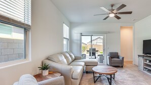 A modern living room with a sectional sofa, a round coffee table, a grey armchair, and a TV stand. - Maricopa Home w/ Putting Green & Covered Patio! (Maricopa)