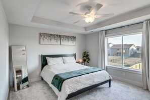 Relax in this serene bedroom with a large bed, ceiling fan, and window offering a view of the outside.