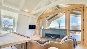 Een modern interieur met een houten plafond, een open haard en grote ramen met uitzicht op de omgeving.