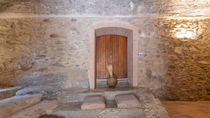 A stone-walled room with a wooden door, a vase, and two cushions on a stone bench.