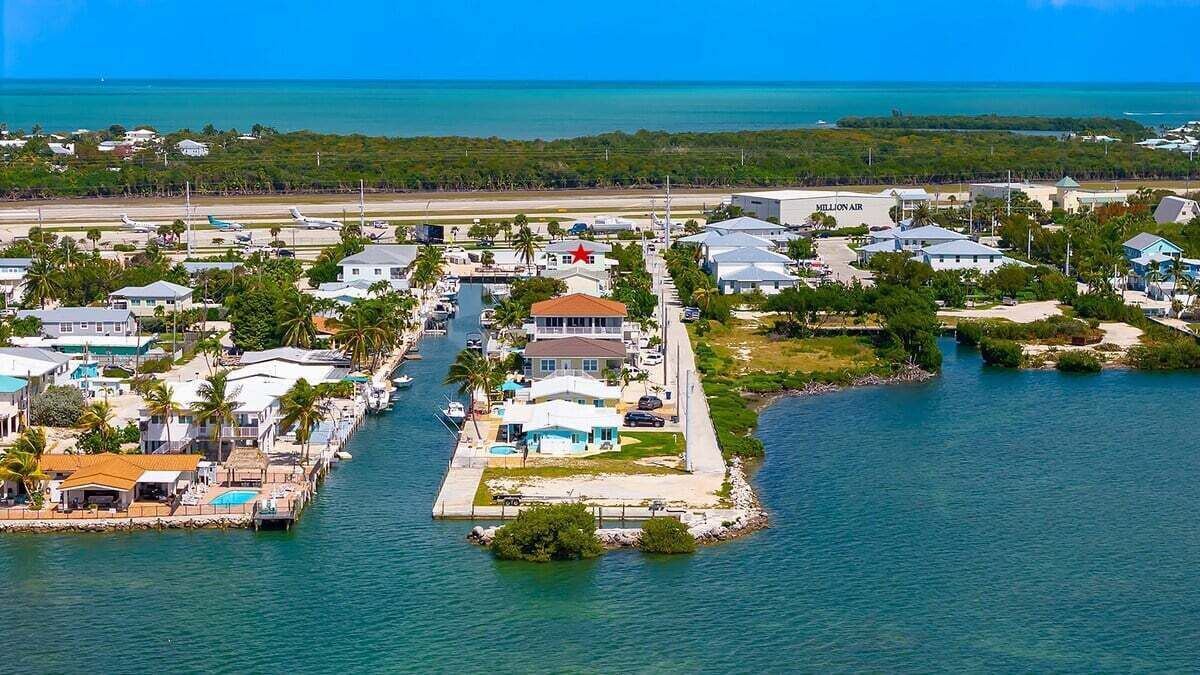 An aerial view of a coastal residential area with houses, a marina, and a clear view of the ocean.