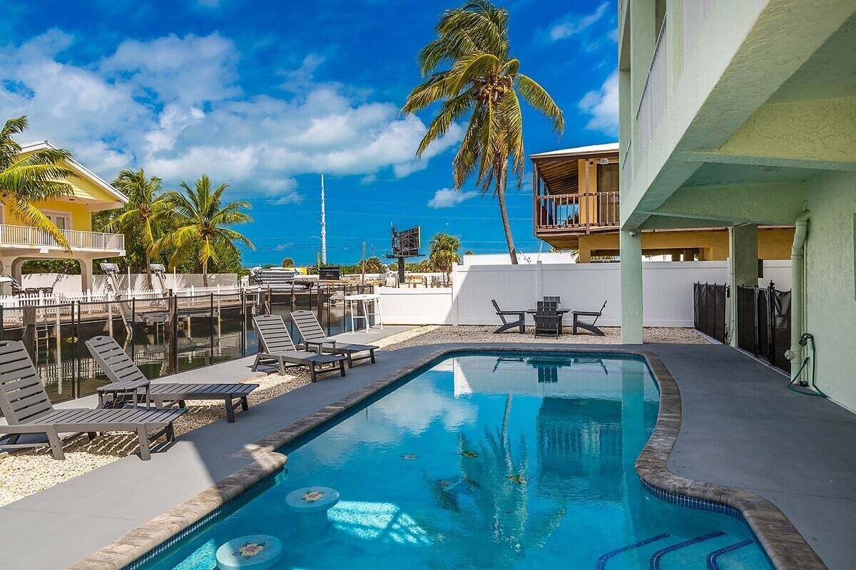 A swimming pool with lounge chairs and a palm tree, surrounded by buildings.
