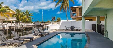 A swimming pool with lounge chairs and a palm tree, surrounded by buildings.