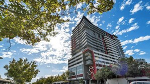 Un hotel moderno de varios pisos con una fachada distintiva en rojo y blanco, situado en una calle concurrida con coches y un autobús.